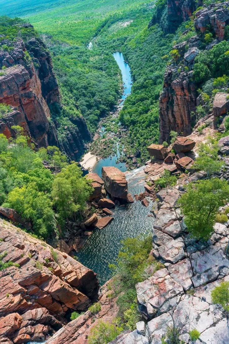 This may contain: a river running through a lush green valley surrounded by rocky cliffs and trees in the distance