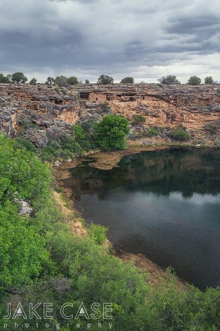 This may contain: a lake surrounded by trees and cliffs under a cloudy sky