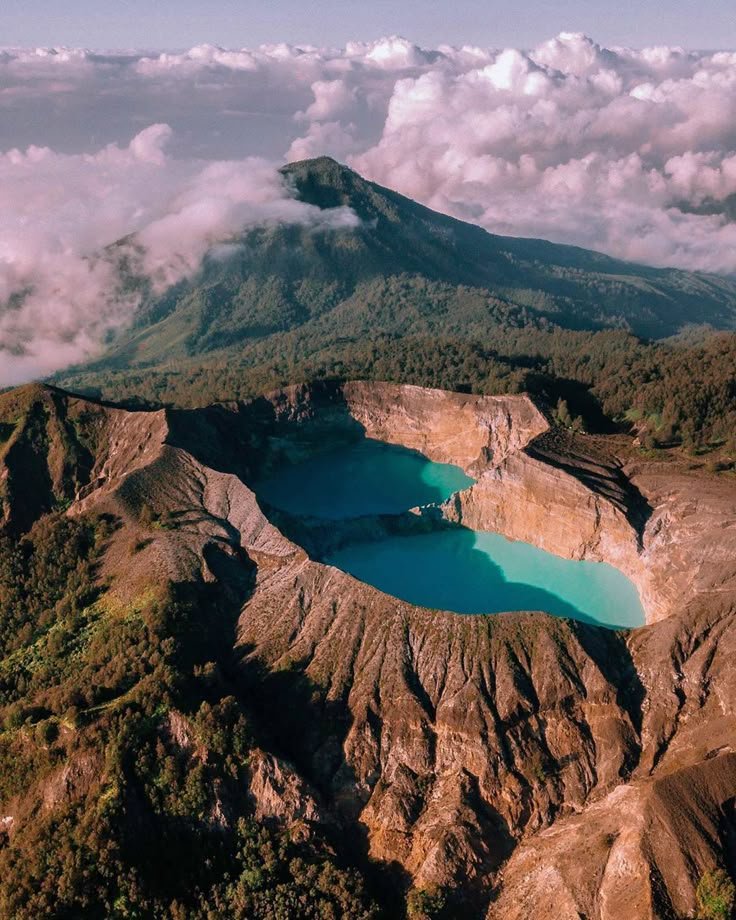 This may contain: an aerial view of a lake surrounded by mountains and clouds in the distance with blue water