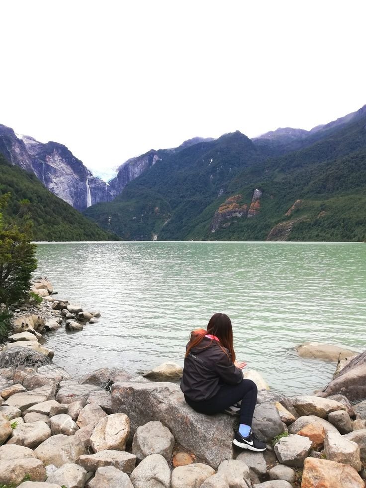 This may contain: a person sitting on rocks near the water