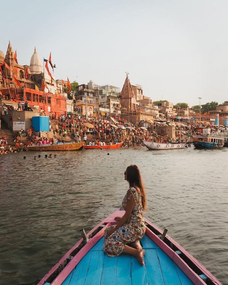 This may contain: a woman sitting on the bow of a boat in front of a crowded river filled with boats