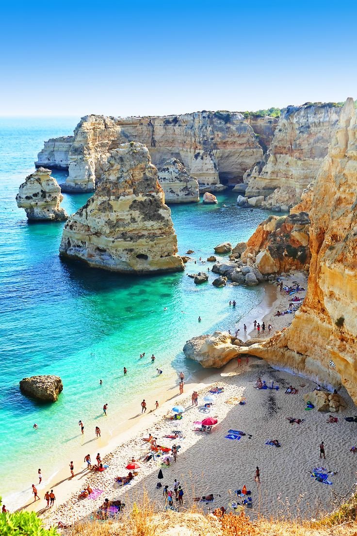 This may contain: the beach is crowded with people on it and there are many cliffs in the background