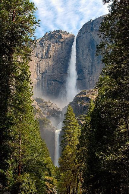 This may contain: the waterfall is surrounded by trees and clouds