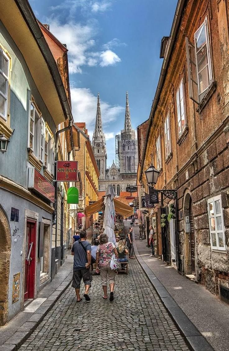 This may contain: people are walking down an old cobblestone street