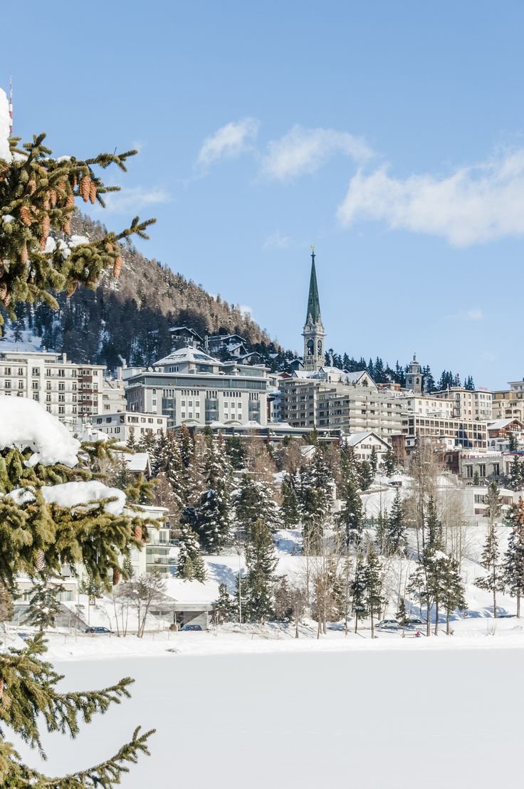 This may contain: a snowy landscape with trees and buildings in the background