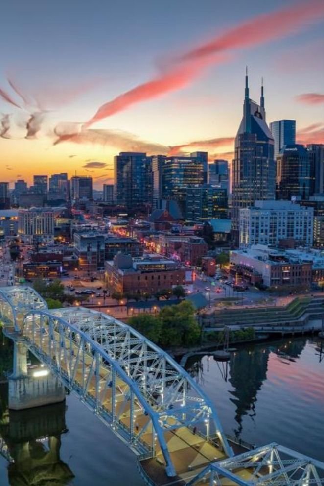 This may contain: an aerial view of a city at sunset with a bridge and river in the foreground