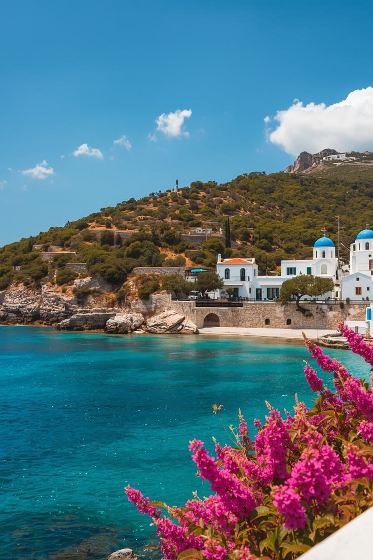 This may contain: the water is blue and clear with white buildings on it, along with purple flowers