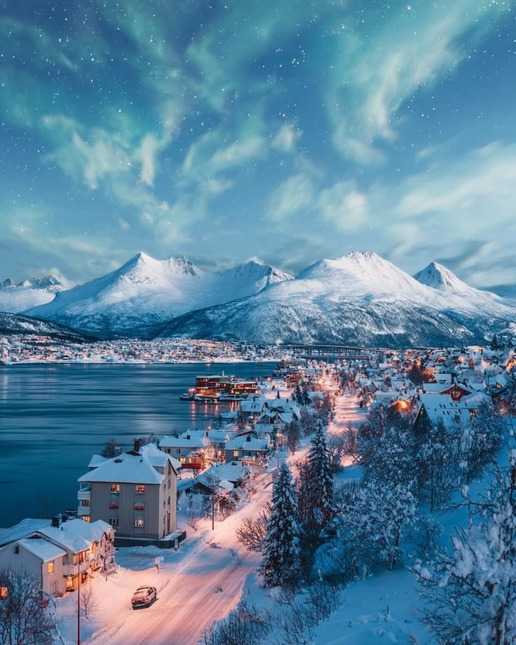 This may contain: the town is surrounded by snow covered mountains and lake at night with stars in the sky