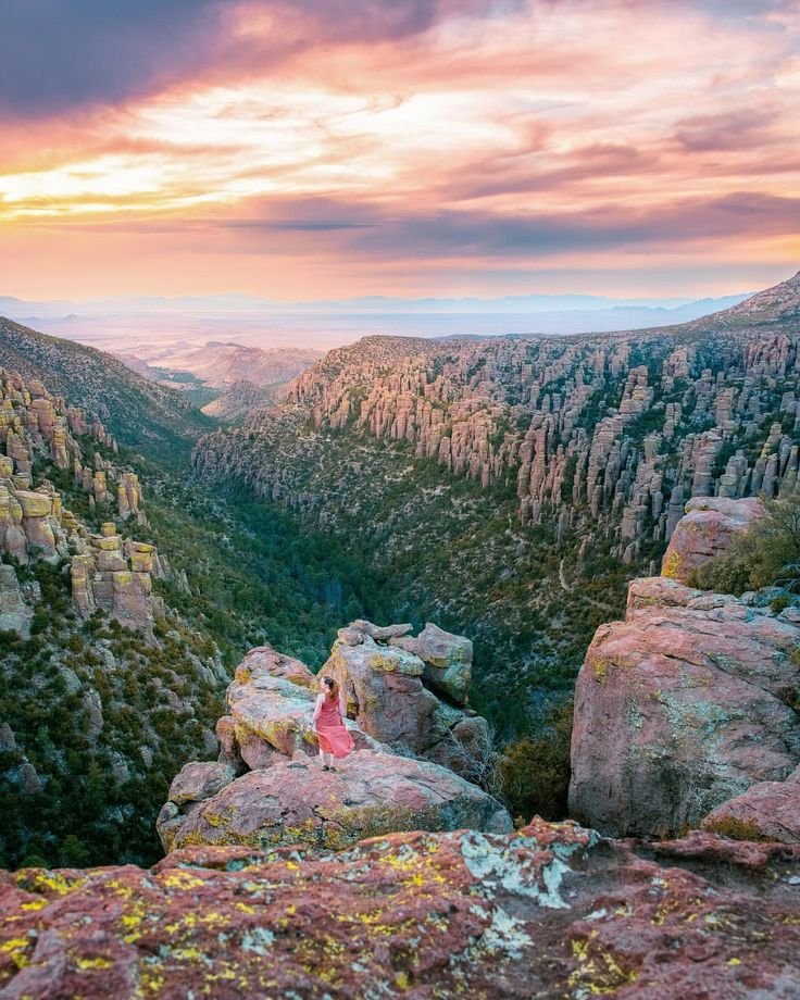 This may contain: a woman sitting on top of a large rock next to a valley filled with trees