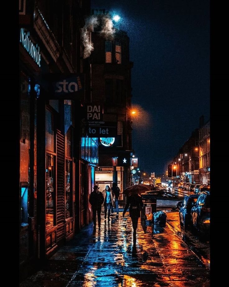 This may contain: people walking down the street in the rain at night