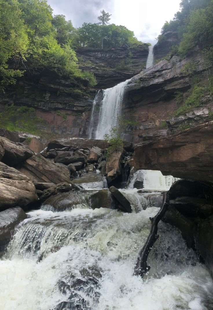 This may contain: a large waterfall is coming down the side of a mountain with rocks and trees around it