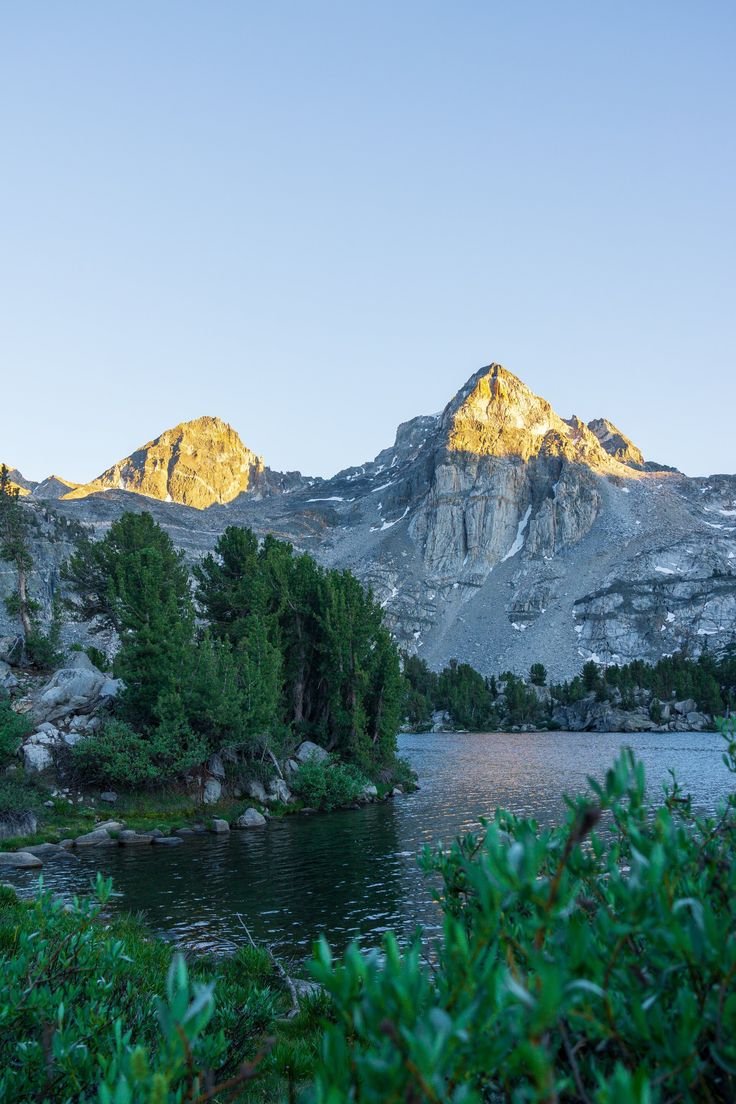This may contain: the mountains are covered in snow and green plants near a lake with water below them