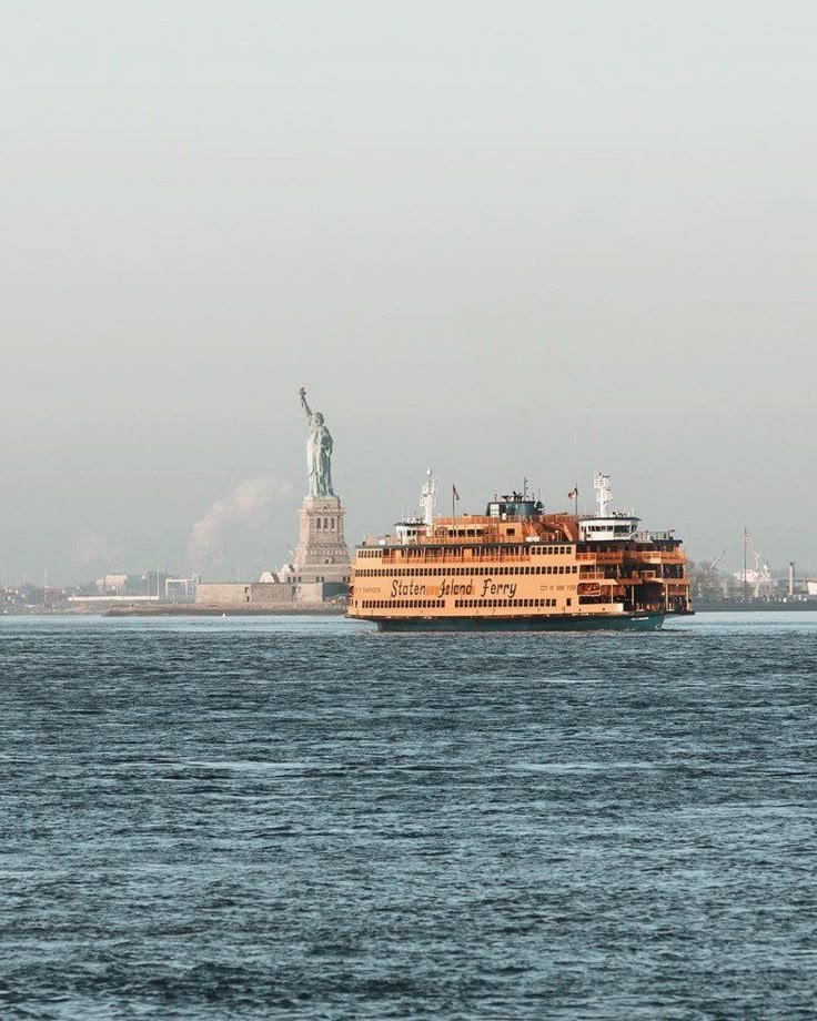This may contain: a large boat floating on top of a body of water near a statue of liberty