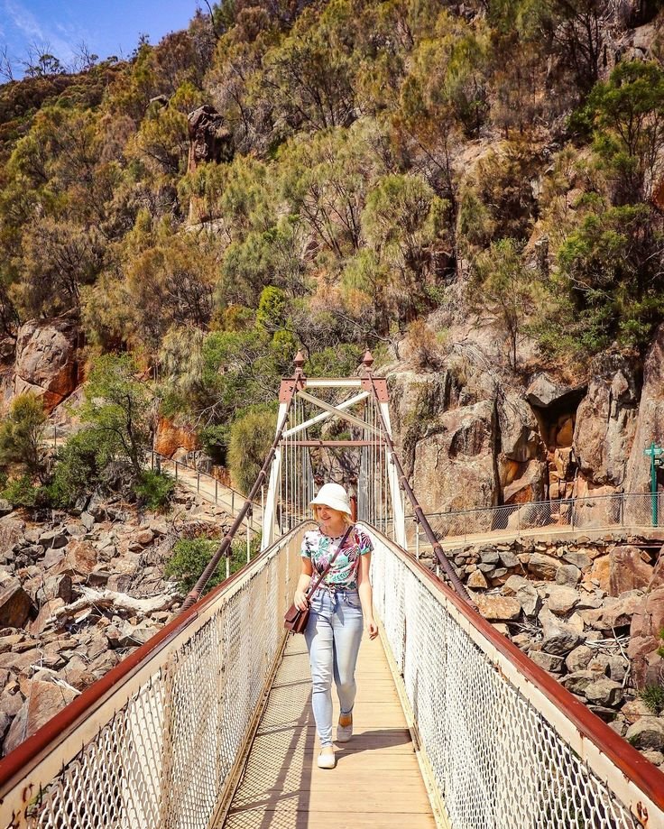 This may contain: a woman walking across a suspension bridge in the mountains