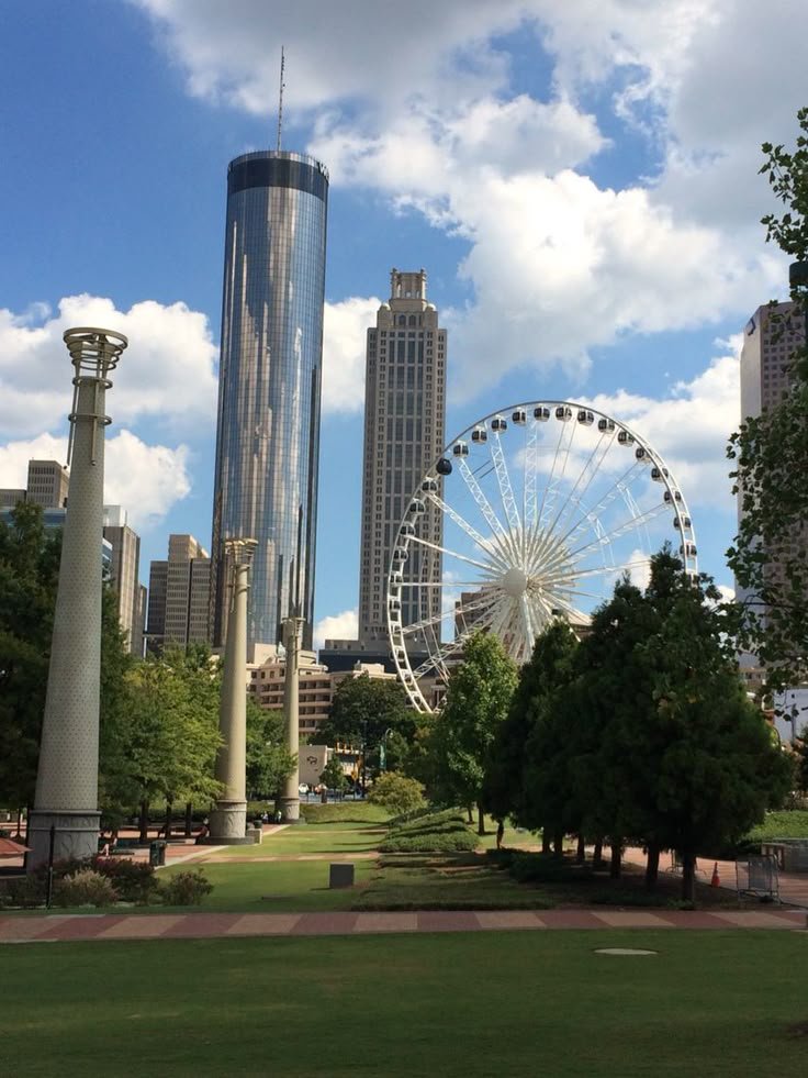 This may contain: a large ferris wheel sitting in the middle of a lush green park next to tall buildings