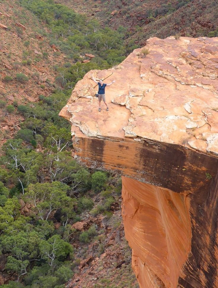 This may contain: a man standing on the edge of a cliff with his arms in the air above him