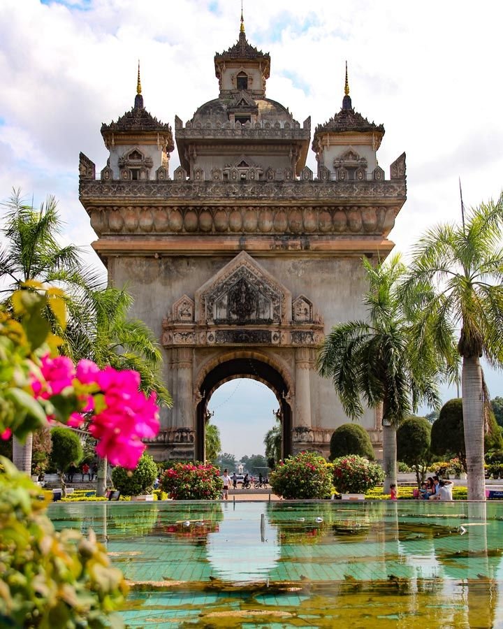 This may contain: the entrance to an ornately designed park with water and flowers in front of it
