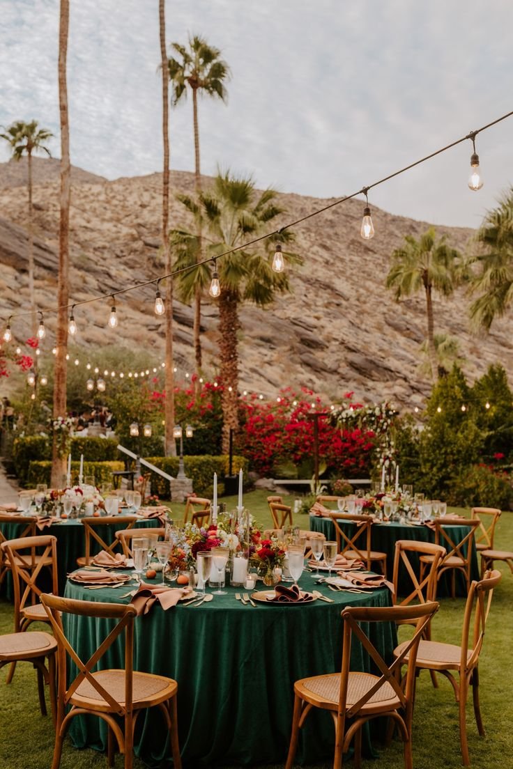 This may contain: an outdoor dining area with palm trees and green tablecloths, surrounded by greenery