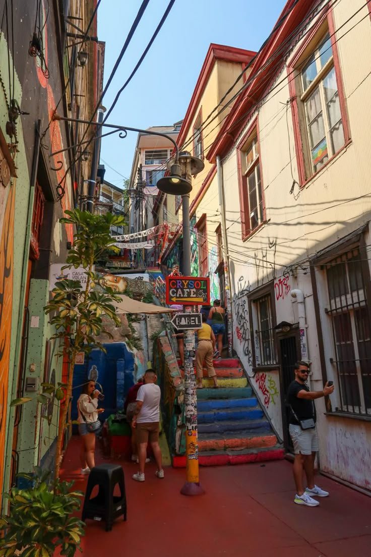 This may contain: several people are walking down the street in an alleyway with colorful stairs and graffiti on the walls