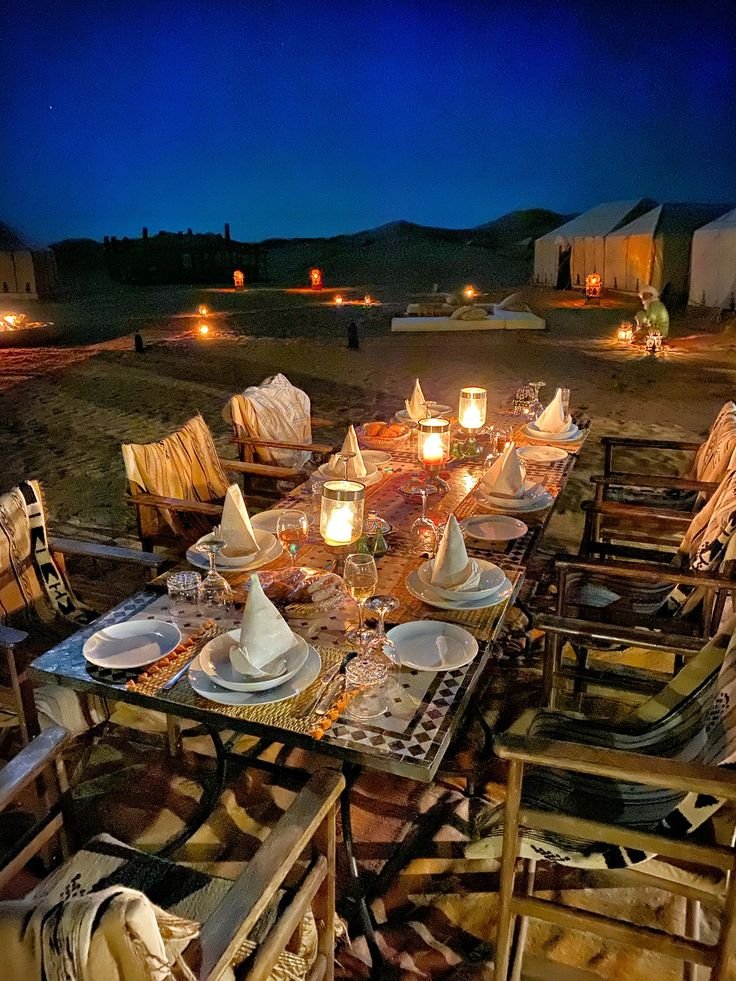 This may contain: a table set up with candles and plates in the middle of a field at night