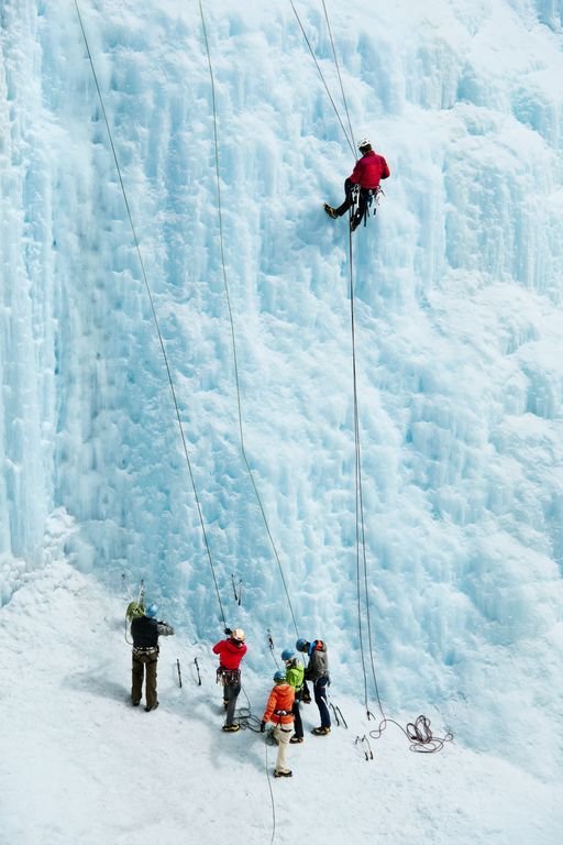 This may contain: several people climbing up the side of an ice - covered mountain with ropes attached to them