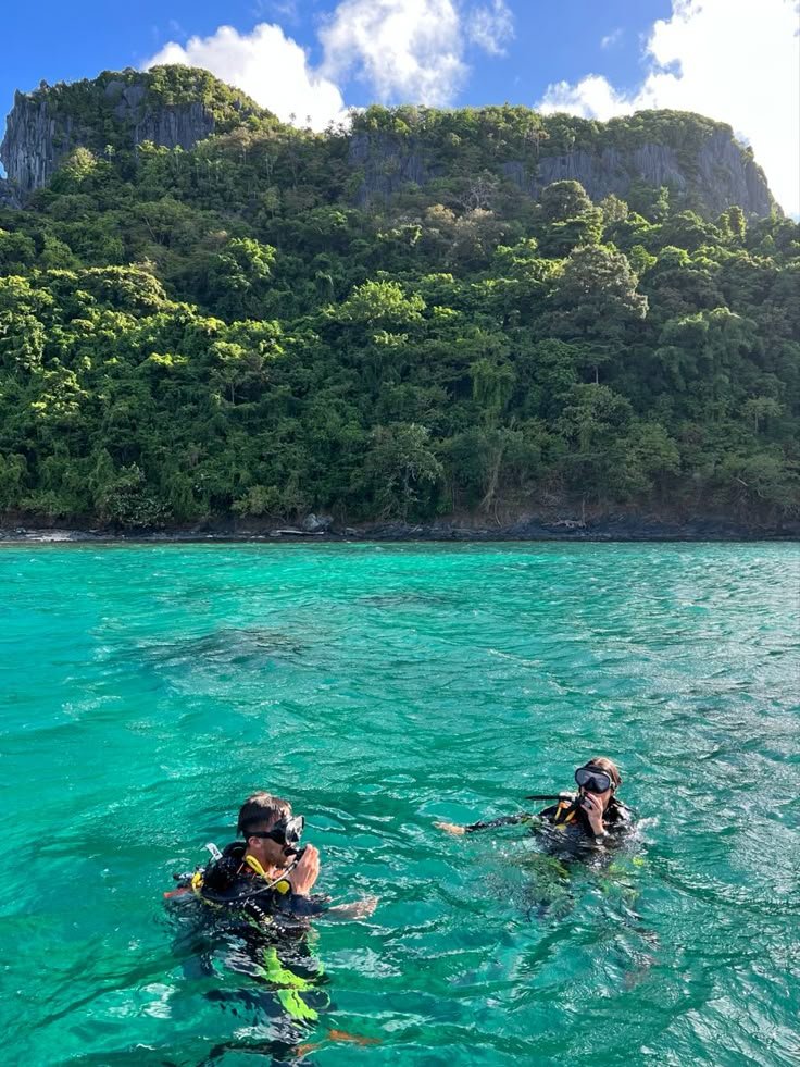 This may contain: two people swimming in the ocean with mountains in the background