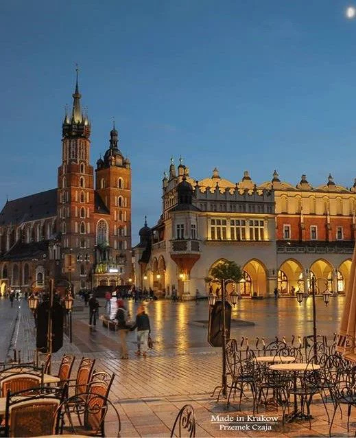 This may contain: an old town square with tables and chairs in the rain at night, surrounded by tall buildings