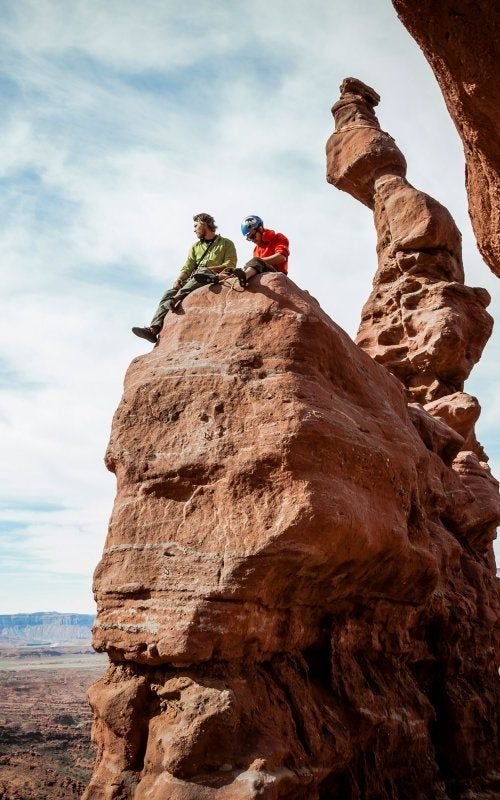 This may contain: two people sitting on top of a large rock formation in the middle of an arid area