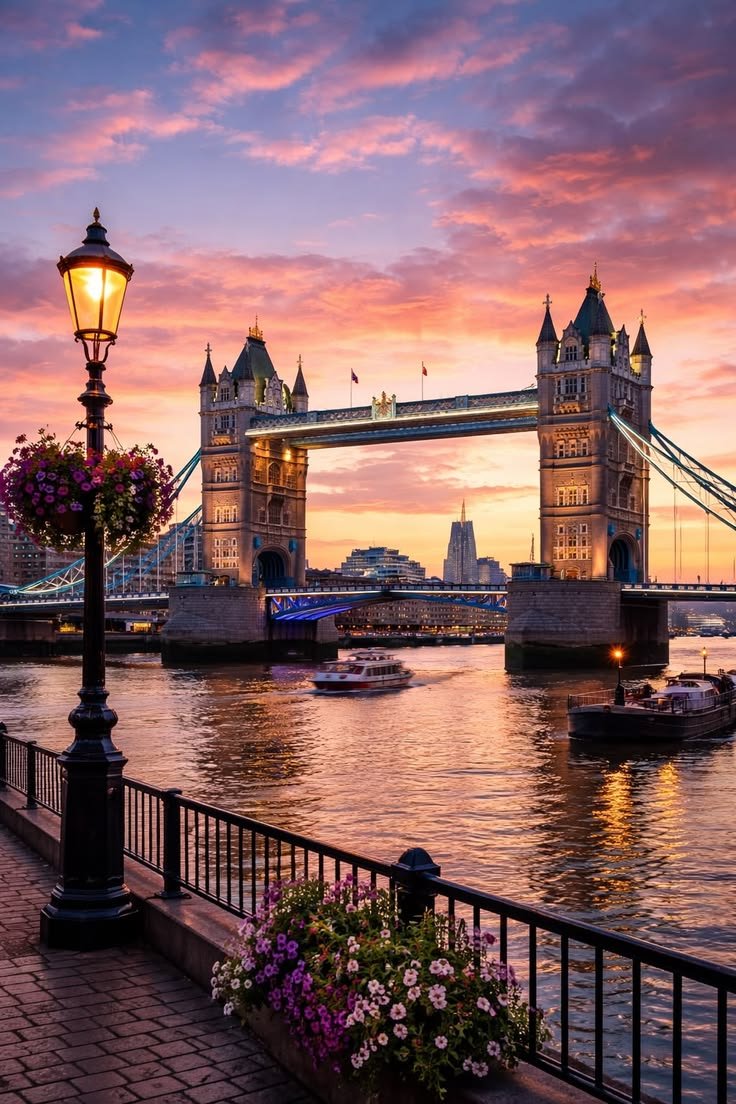 This may contain: the tower bridge in london is lit up at night with pink and purple clouds above it