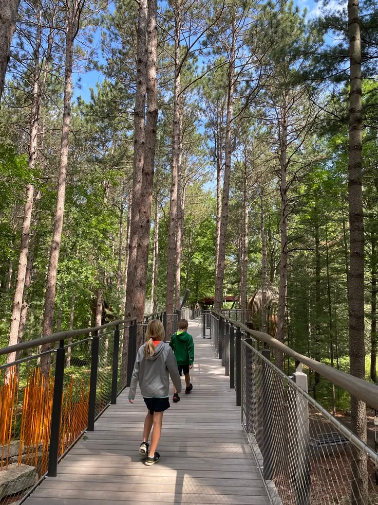 This may contain: two people walking across a bridge in the woods