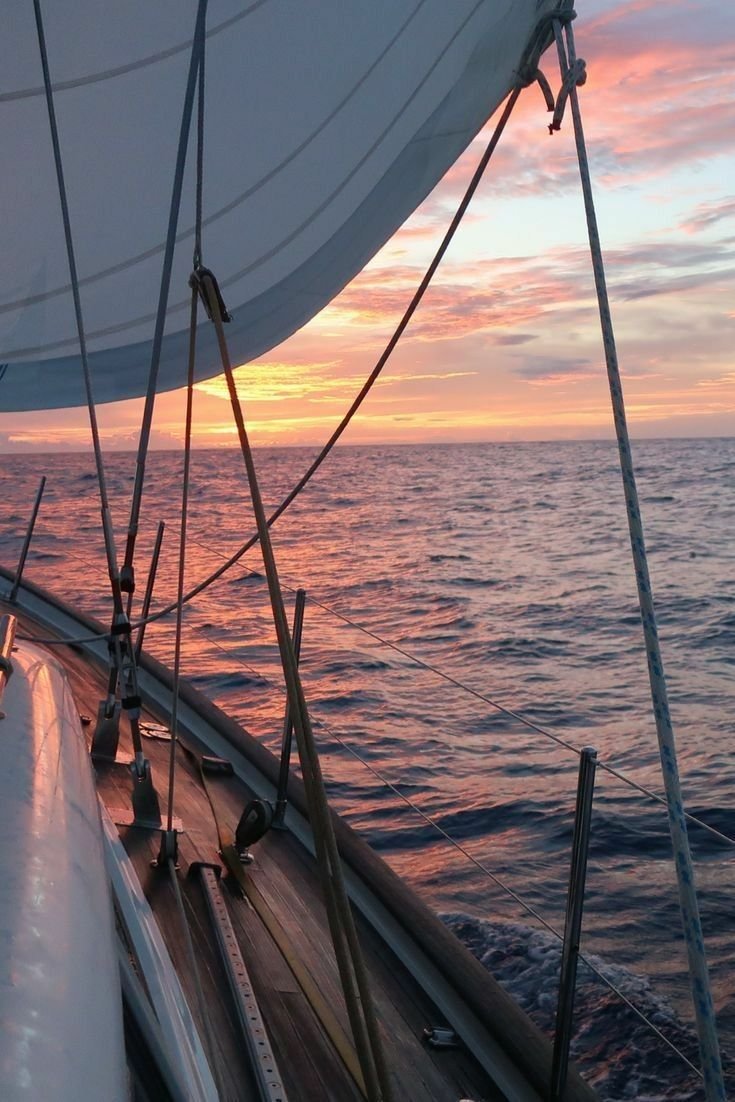 This may contain: the sun is setting over the ocean on a sailboat