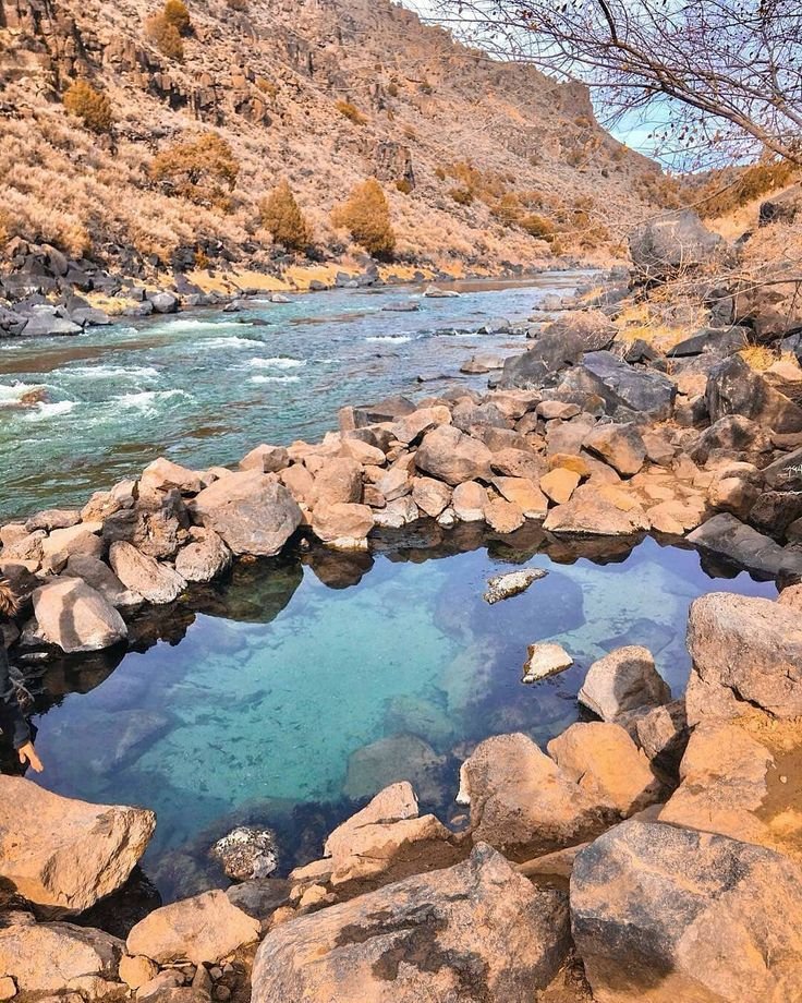 This may contain: a man standing on rocks next to a river with clear water surrounded by rocky mountains