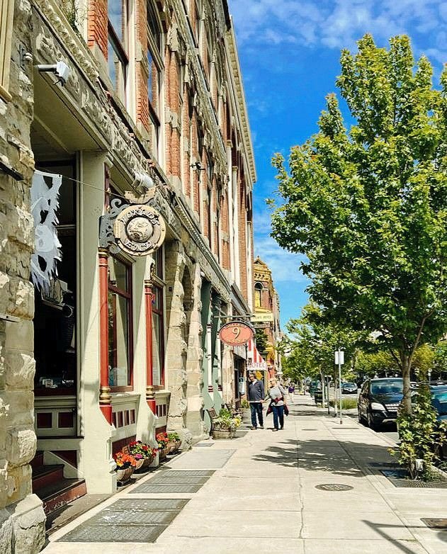 This may contain: two people walking down the sidewalk in front of an old building on a sunny day