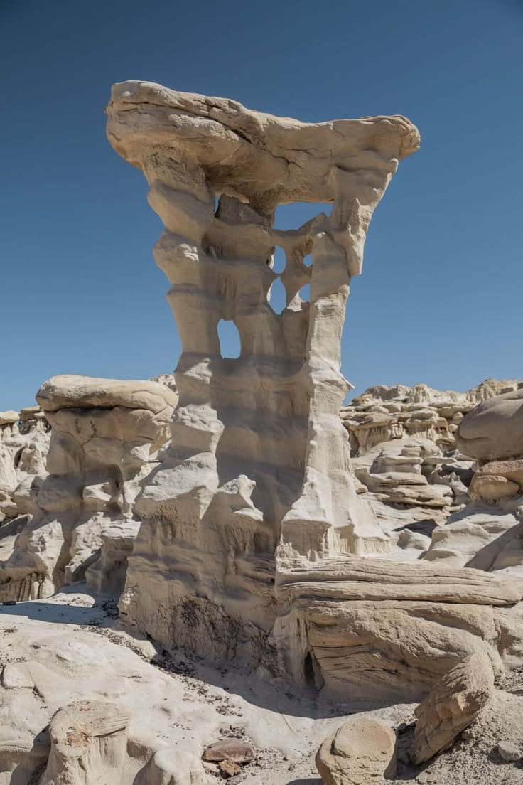 This may contain: a rock formation in the middle of a desert with blue skies above it and rocks below