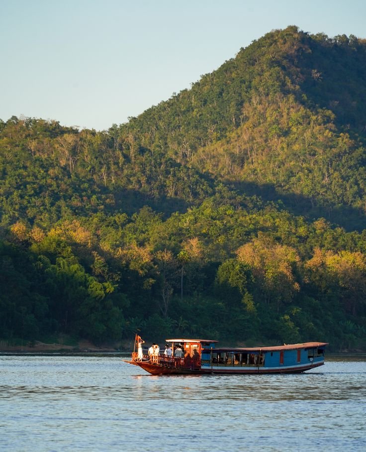 This may contain: a boat with people on it is in the water near some hills and trees,