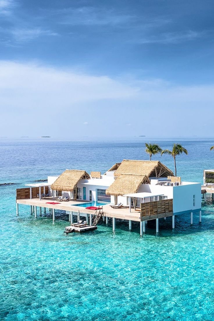 This may contain: the water is crystal blue and there are two houses on stilts in the ocean