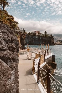 This may contain: a pier with chairs and umbrellas on the shore next to the ocean in front of a cliff