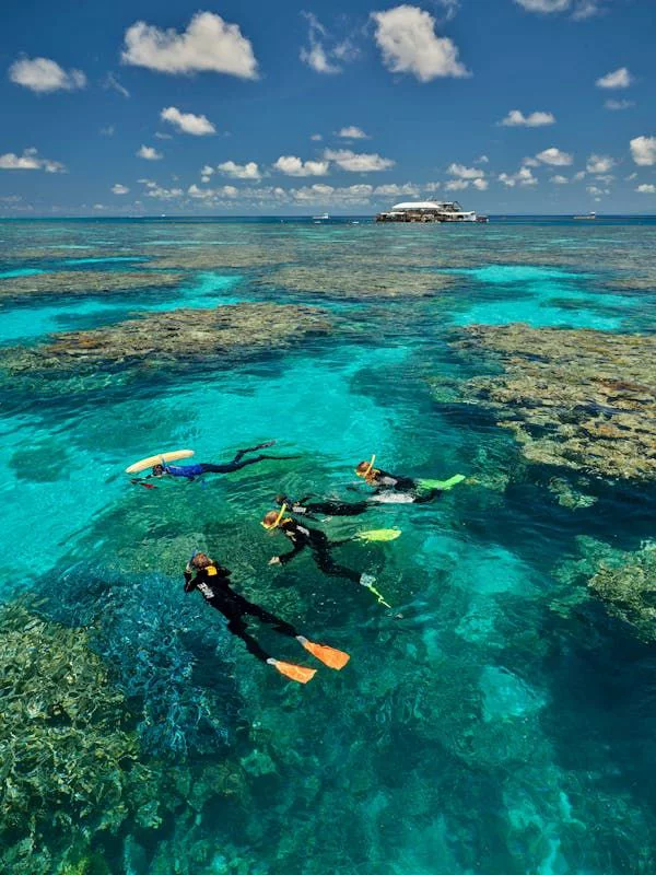 This may contain: two people snorkeling in the clear blue water near an island with a boat