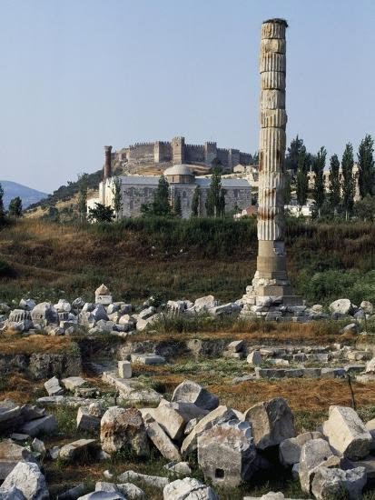 This may contain: an ancient column in the middle of a field with large rocks and trees around it