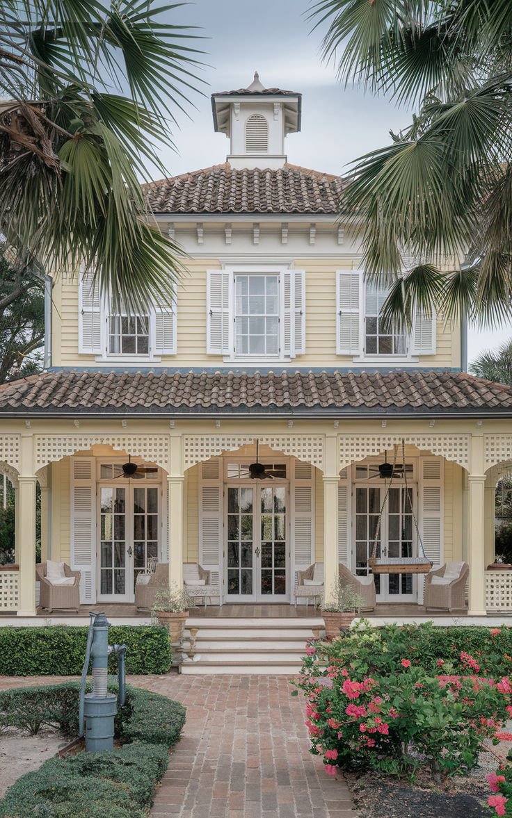 This may contain: a yellow house with palm trees and flowers around it