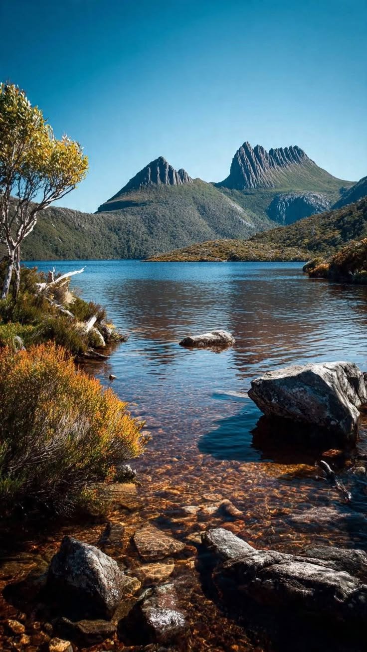 This may contain: a lake surrounded by mountains with rocks in the water