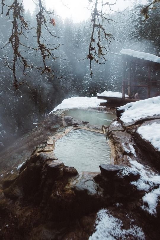 This may contain: a hot tub surrounded by snow covered rocks