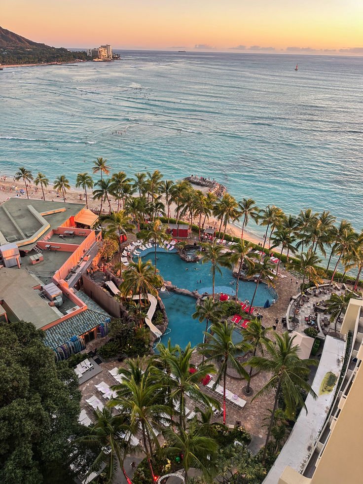 This may contain: an aerial view of the beach and pool area at sunset with palm trees in the foreground