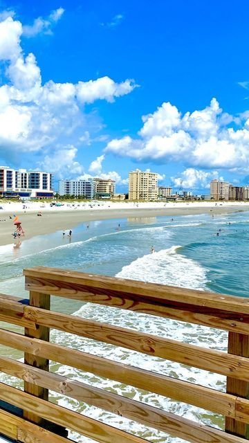 This may contain: a beach with people walking on the sand and buildings in the background