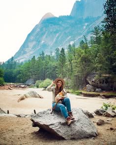 This may contain: a woman sitting on top of a large rock holding a small dog in her arms
