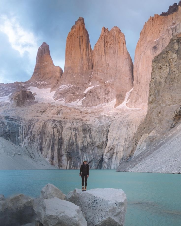 This may contain: a man standing on top of a large rock next to a lake and mountain range
