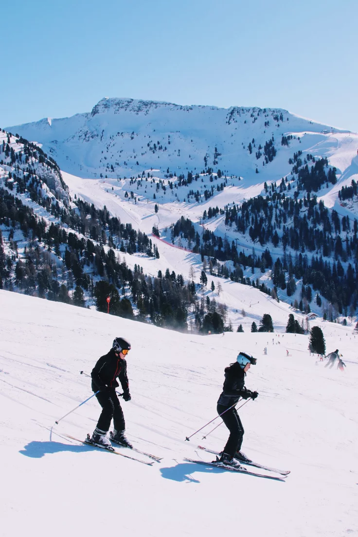 This may contain: two people on skis in the snow with mountains in the backgrouund
