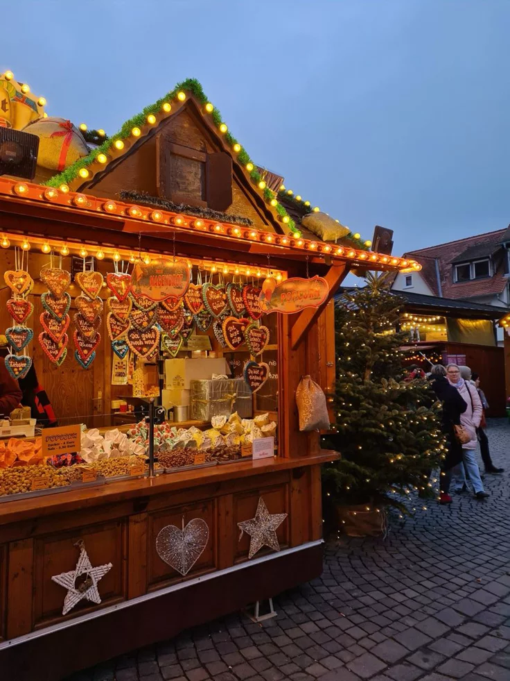 This may contain: an outdoor christmas market with lights on the roof and decorations hanging from it's roof