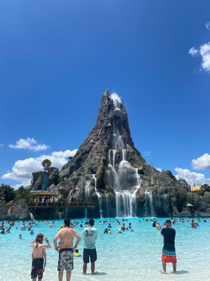 This may contain: people are standing in the water at an amusement park with a large waterfall behind them