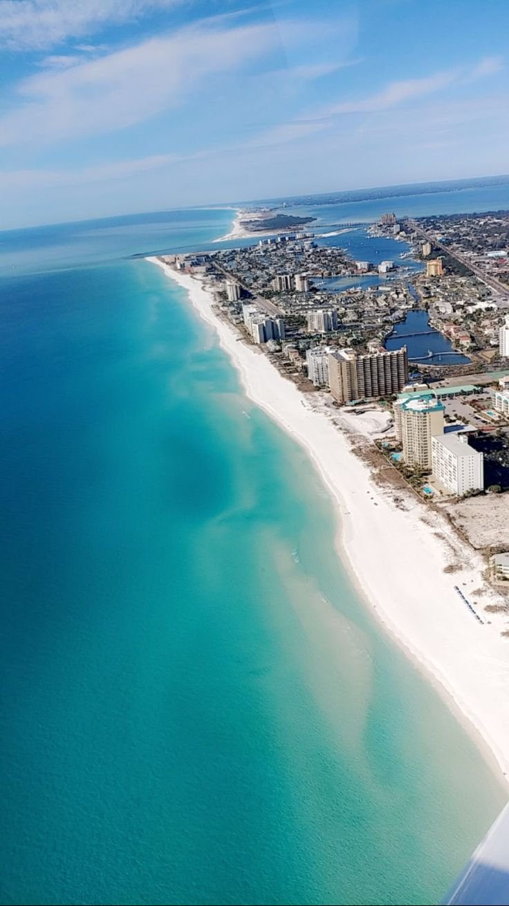 This may contain: an aerial view of the beach and ocean from above, with buildings in the background